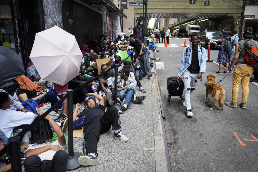 Migrants sit in a queue outside of The Roosevelt Hotel that is being used by the city as temporary housing, Monday, July 31, 2023, in New York. Beleaguered by a continuing influx of asylum seekers, New York City Mayor Eric Adams is further tightening shelter rules by limiting adult migrants to just 30 days — to help ease pressures on the city's already struggling shelter system and perhaps dissuade more migrants from coming.(AP Photo/John Minchillo, File)