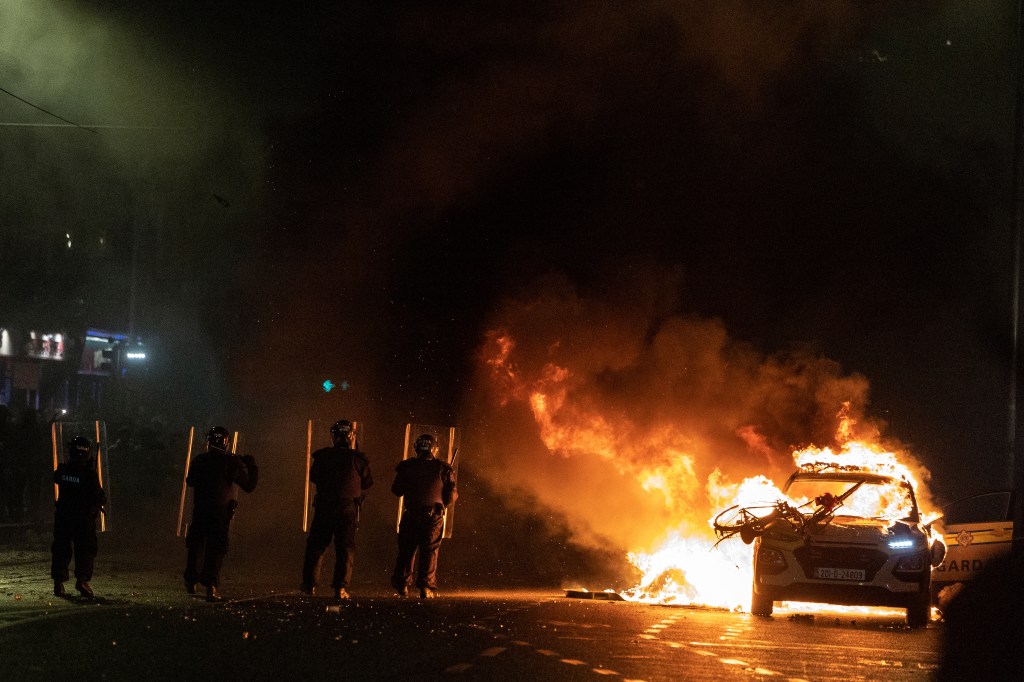 Riot police officers face down demonstrators next to a burning police car near a crime scene of a school stabbing that left several children and adults injured, in Dublin, Ireland, November 23, 2023. REUTERS/Clodagh Kilcoyne