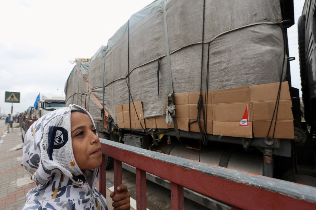 A child looks at trucks carrying aid waiting to head towards north Gaza during a temporary truce between Hamas and in Israel, in the central Gaza Strip, November 27, 2023. REUTERS/Ibraheem Abu Mustafa      TPX IMAGES OF THE DAY